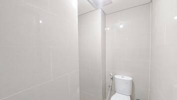 Un baño moderno con azulejos blancos, un inodoro, una ducha y un cubo de basura de vidrio.