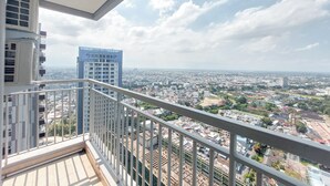 A balcony with a metal railing overlooking a cityscape with various buildings and a clear sky. - Serene And Comfort Living 3Br At Podomoro City Deli Medan Apartment (Medan)