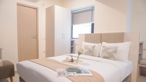 A modern bedroom with a large bed, a bedside table with a vase and candle, and a window with blinds.