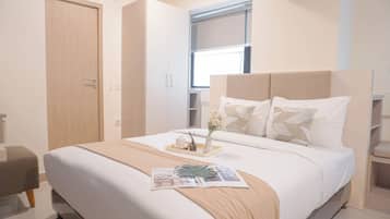 A modern bedroom with a large bed, a bedside table with a vase and candle, and a window with blinds.