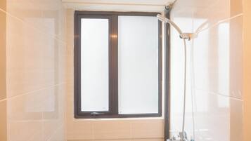 A bathroom with a window, a shower, and tiled walls.