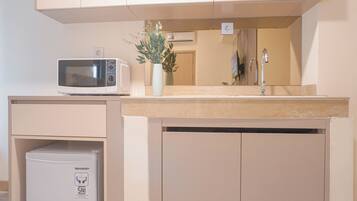 A kitchenette with a microwave, a small refrigerator, a sink, and a vase with flowers.