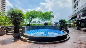 A rooftop swimming pool with a checkered pattern, surrounded by potted plants and trees, with buildings in the background. - Comfortable And Homey Studio Room Parkland Avenue Apartment (South Tangerang)