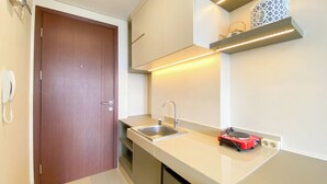 A small kitchenette with a wooden door, a sink, a kettle, and a shelf with a kettle. - Comfortable And Homey Studio Room Parkland Avenue Apartment (South Tangerang)
