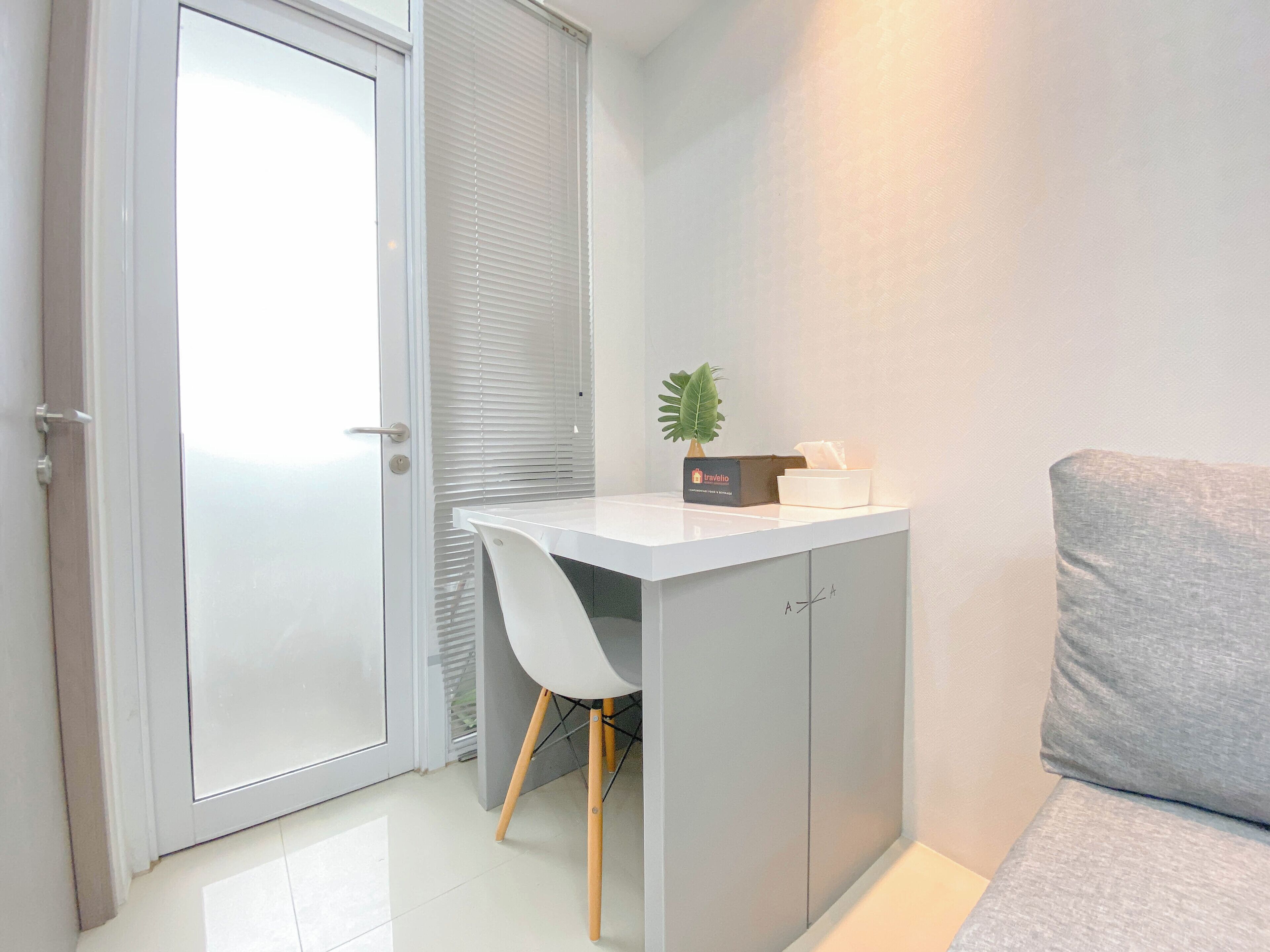 A compact, modern room with a white desk, a chair, a grey sofa, and a door with a frosted glass panel.