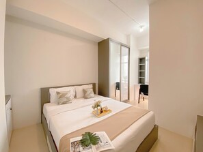 Un dormitorio moderno con una cama grande, una mesita de noche con un florero y una bandeja, y un armario con espejo.