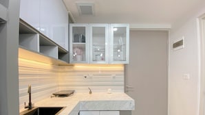 A modern kitchen with white cabinetry, a marble countertop, and under-cabinet lighting. - Cozy 1Br With Extra Room At Vasanta Innopark Apartment (Cikarang)