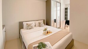 A modern bedroom with a large bed, a bedside table with a tray, and a view of a balcony. - Cozy 1Br With Extra Room At Vasanta Innopark Apartment (Cikarang)