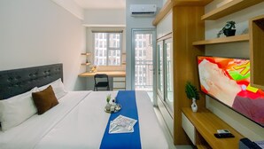 A hotel room with a bed, a desk, a TV, and a window with a city view. - Cozy And Enjoy Living Studio Transpark Juanda Bekasi Timur Apartment (Bekasi)