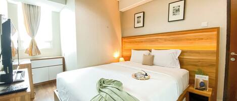 A hotel room with a wooden headboard, a bed with white bedding, a bedside table with a lamp, and a small plant.