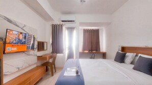 A hotel room with a bed, a desk, a chair, a TV mounted on the wall, and a window with curtains. - Good And Homey Studio Apartment Urban Heights Residences (South Tangerang)