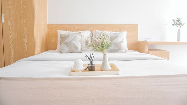 A neatly made bed with a wooden headboard, two pillows, a tray with a vase of flowers, and a small bottle. - Good Choice Studio Apartment Tamansari Mahogany Karawang (Karawang)