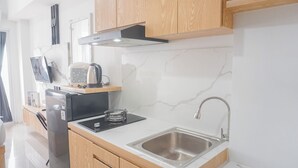 A modern kitchen with wooden cabinets, a stainless steel sink, a built-in stove, and a coffee maker. - Good Choice Studio Apartment Tamansari Mahogany Karawang (Karawang)