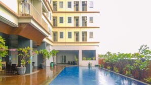 A swimming pool with a tiled deck, surrounded by potted plants and a multi-story building with balconies. - Good Choice Studio Apartment Tamansari Mahogany Karawang (Karawang)