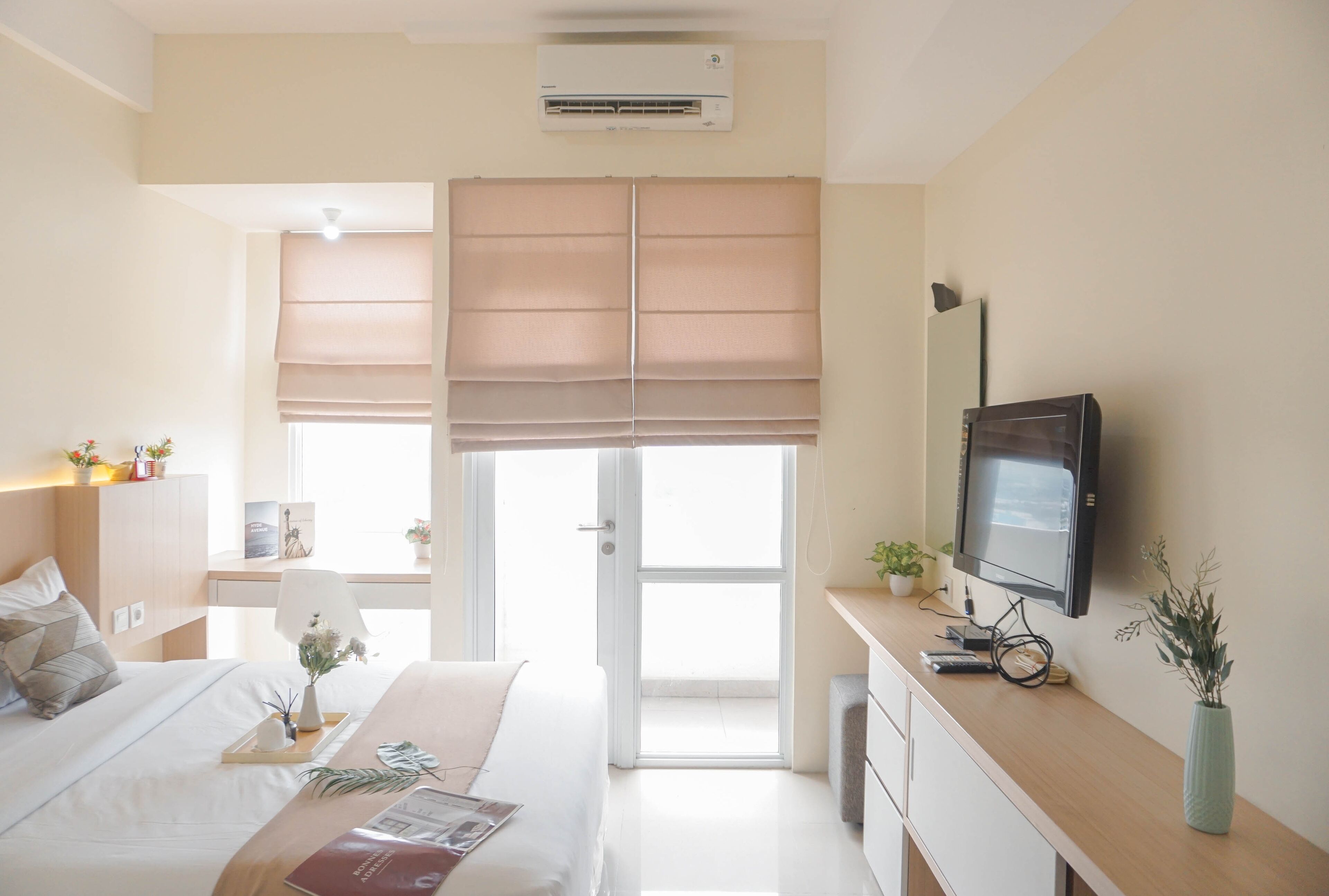 A modern bedroom with a bed, bedside table, TV, and a window with blinds.