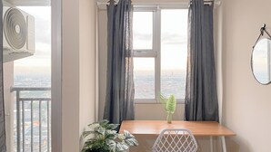 A room with a window, a table, a chair, a potted plant, and a wall-mounted mirror. - Relaxing Studio Apartment At Transpark Juanda Bekasi Timur (Bekasi)
