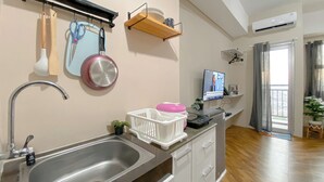 A modern kitchen with a stainless steel sink, wooden utensils, a pink colander, and a TV on a stand. - Relaxing Studio Apartment At Transpark Juanda Bekasi Timur (Bekasi)