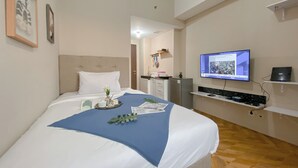 A hotel room with a bed, a television, a desk, and a kitchenette. - Relaxing Studio Apartment At Transpark Juanda Bekasi Timur (Bekasi)