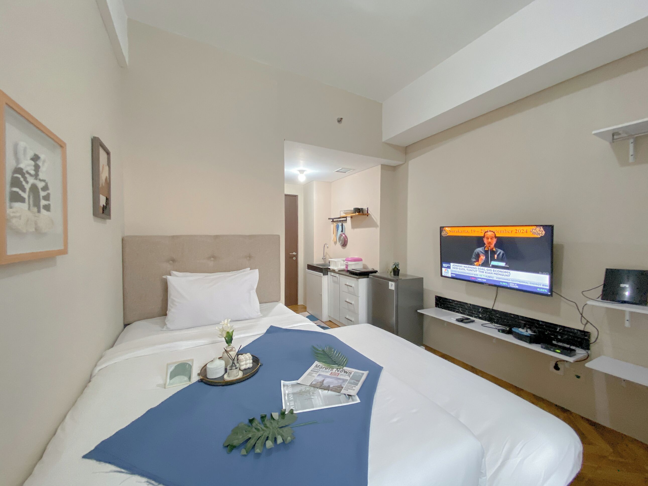 A hotel room with a bed, a television, a desk, and a small kitchenette.