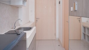 A modern kitchen with a sink, cabinets, and a door. - Cozy Studio Apartment Tree Park City Bsd (South Tangerang)