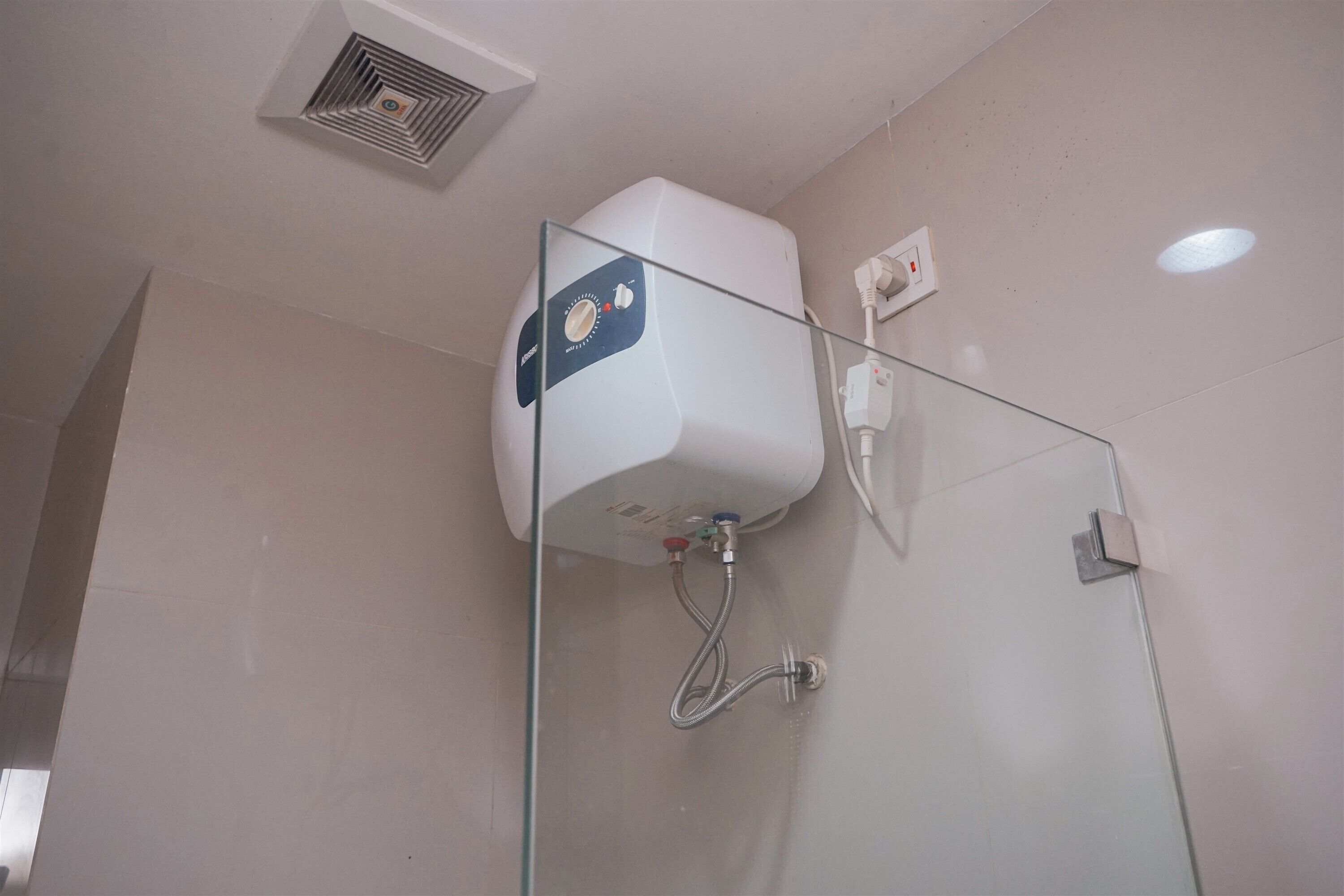 A bathroom with a glass shower enclosure, a white ceiling vent, and a wall-mounted heater.