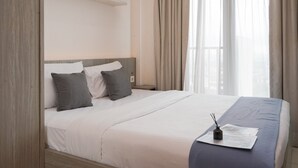 A hotel room with a large bed, a bedside table, a nightstand, and a window with curtains. - Cozy Studio Apartment Tree Park City Bsd (South Tangerang)