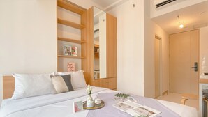 A neatly arranged hotel room with a bed, a bedside table, a mirror, and a wardrobe. - Warm And Good Studio Room At Tokyo Riverside Pik 2 Apartment (Teluknaga)