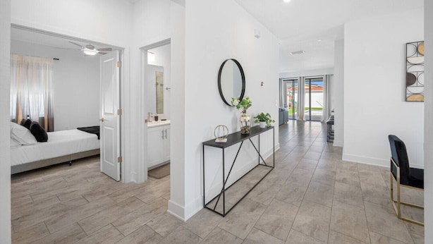 A modern interior with a bed, a console table with decorative items, and a hallway leading to a door. - Luxe Villa • Pool • Spa • Fire Pit • Games & More! (Tampa)