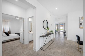 Un intérieur moderne comprenant un lit, une console agrémentée d’objets décoratifs et un couloir menant à une porte.