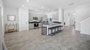 A modern kitchen with white cabinets, stainless steel appliances, and a central island with bar stools. - Luxe Villa • Pool • Spa • Fire Pit • Games & More! (Tampa)