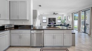 A modern kitchen with grey cabinets, a dishwasher, a built-in oven, and a large island with a sink. - Luxe Villa • Pool • Spa • Fire Pit • Games & More! (Tampa)