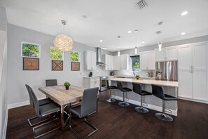 A modern kitchen with white cabinets, a wooden dining table, and bar stools.