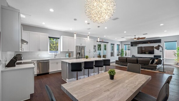 A modern kitchen with white cabinets, a central island with bar stools, a dining table, and a large chandelier. - Tampa Modern Oasis • Pool+Spa • Game Room • Sleeps 16 (Tampa)