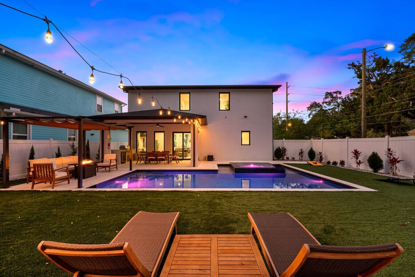 A modern house with a swimming pool, outdoor seating, and string lights.