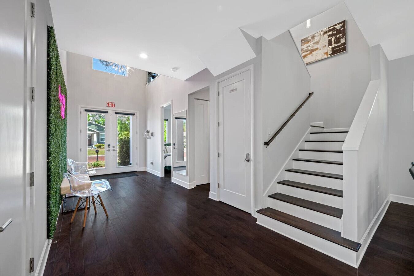 A spacious hallway with a dark wood floor, white walls, and a staircase with a black handrail.