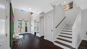 A spacious hallway with a dark wood floor, white walls, and a staircase with a black handrail. - Tampa Modern Oasis • Pool+Spa • Game Room • Sleeps 16 (Tampa)