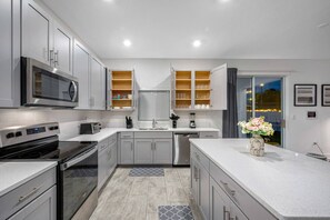 Cozinha moderna com eletrodomésticos de aço inoxidável, armários cinzas e uma ilha central com um vaso de flores.