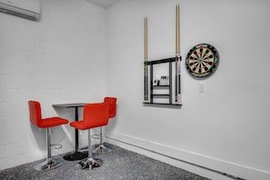 Een kamer met een witte bakstenen muur, een dartbord en twee rode stoelen met een kleine tafel.