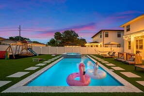 Um quintal com piscina, balneários e um parquinho infantil.