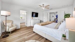 A bedroom with a bed, a chair, a TV, a ceiling fan, and a door leading to another room. - Family Oasis • Pool • Slide • Games • Sleeps 14+ (Tampa)