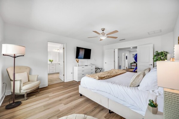 Un dormitorio con cama, ventilador de techo, televisión, lámpara de pie y una silla.