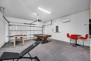 Een kamer met een tafelvoetbaltafel, een pooltafel, een fitnessbank en rode stoelen.