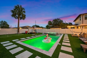 A backyard with a swimming pool, a play area, and a seating area with umbrellas.