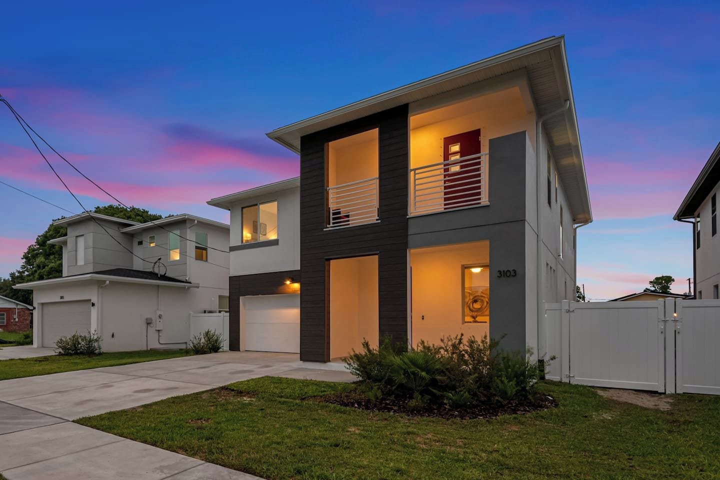 A modern two-story house with a garage, a balcony, and a well-maintained lawn.
