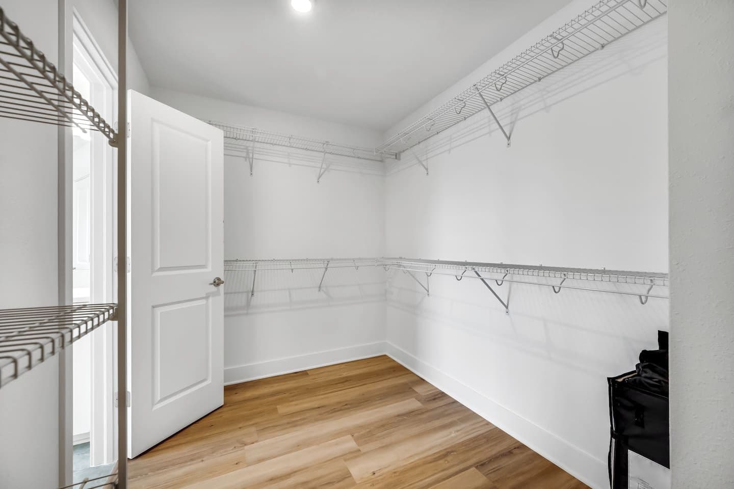A room with a wooden floor, white walls, and a door. There are metal racks on the walls for hanging items.
