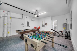 Una habitación con mesa de futbolín, dardos y equipo de ejercicio.