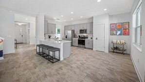 A modern kitchen with grey cabinets, a central island with bar stools, stainless steel appliances, and a small bar area with a sign.