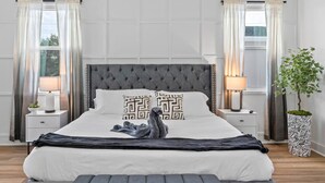 A bedroom with a tufted headboard, two bedside lamps, a potted plant, and a decorative swan on the bed.