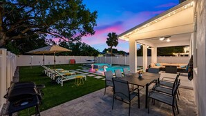 A backyard with a pool, outdoor seating, and a barbecue grill.