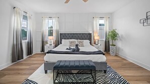 A modern bedroom with a tufted headboard, a zebra-patterned rug, and a ceiling fan.